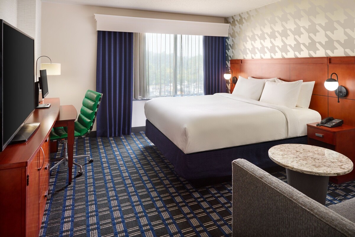 Une chambre d’hôtel comprenant un lit, un bureau avec un ordinateur, une chaise, une petite table et une table de chevet avec une lampe.