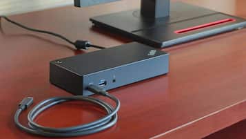 A black electronic device on a wooden surface with a cable connected to it.