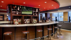 Zona de bar moderna con una barra curva, varios taburetes y una pantalla de televisión mostrando un evento deportivo.
