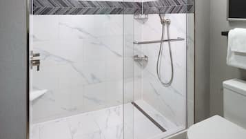 Un bagno moderno con cabina doccia in vetro, piastrelle in marmo bianco e WC a vista.