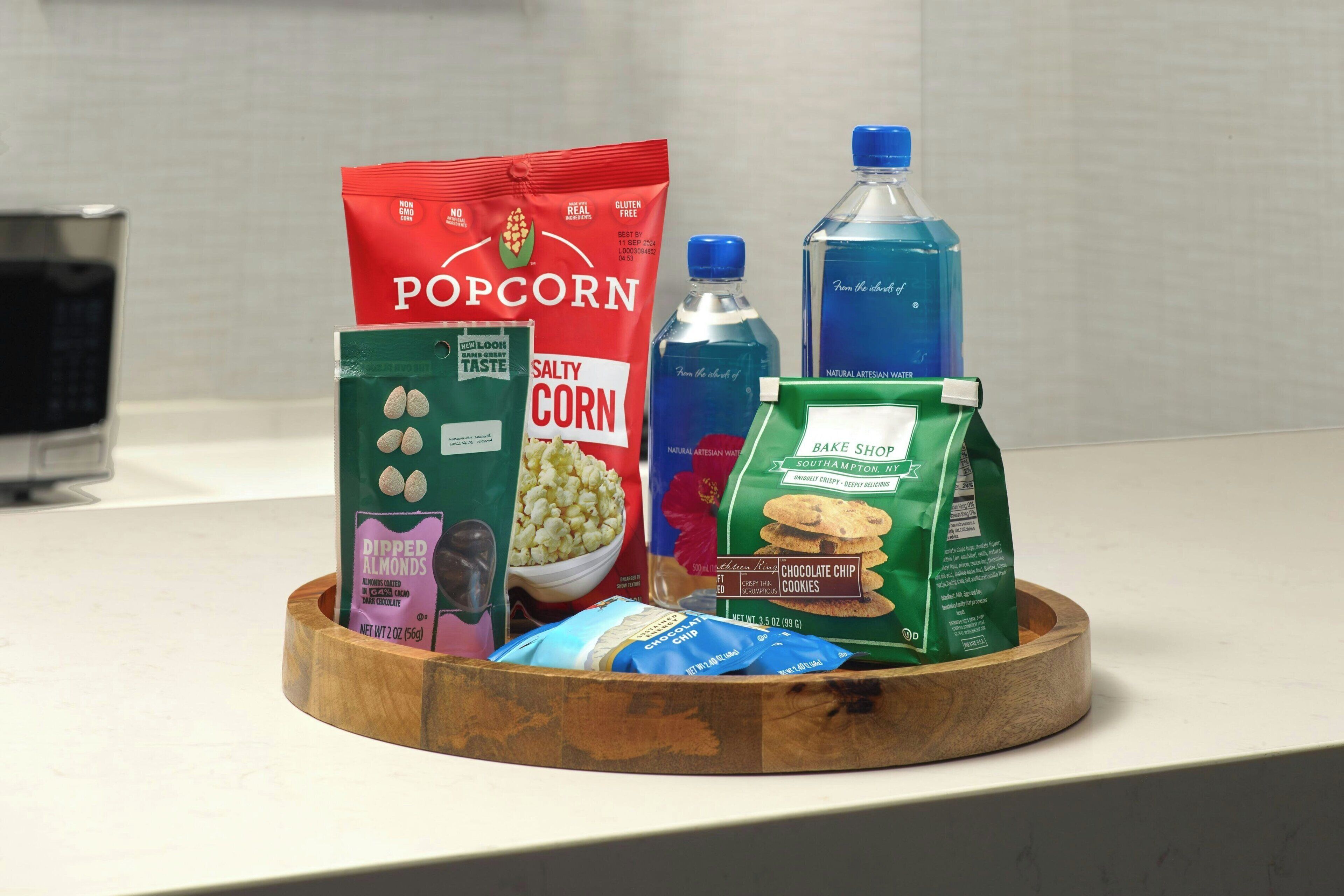 A wooden tray with various snack items including popcorn, chocolate chip cookies, and a bottle of water.