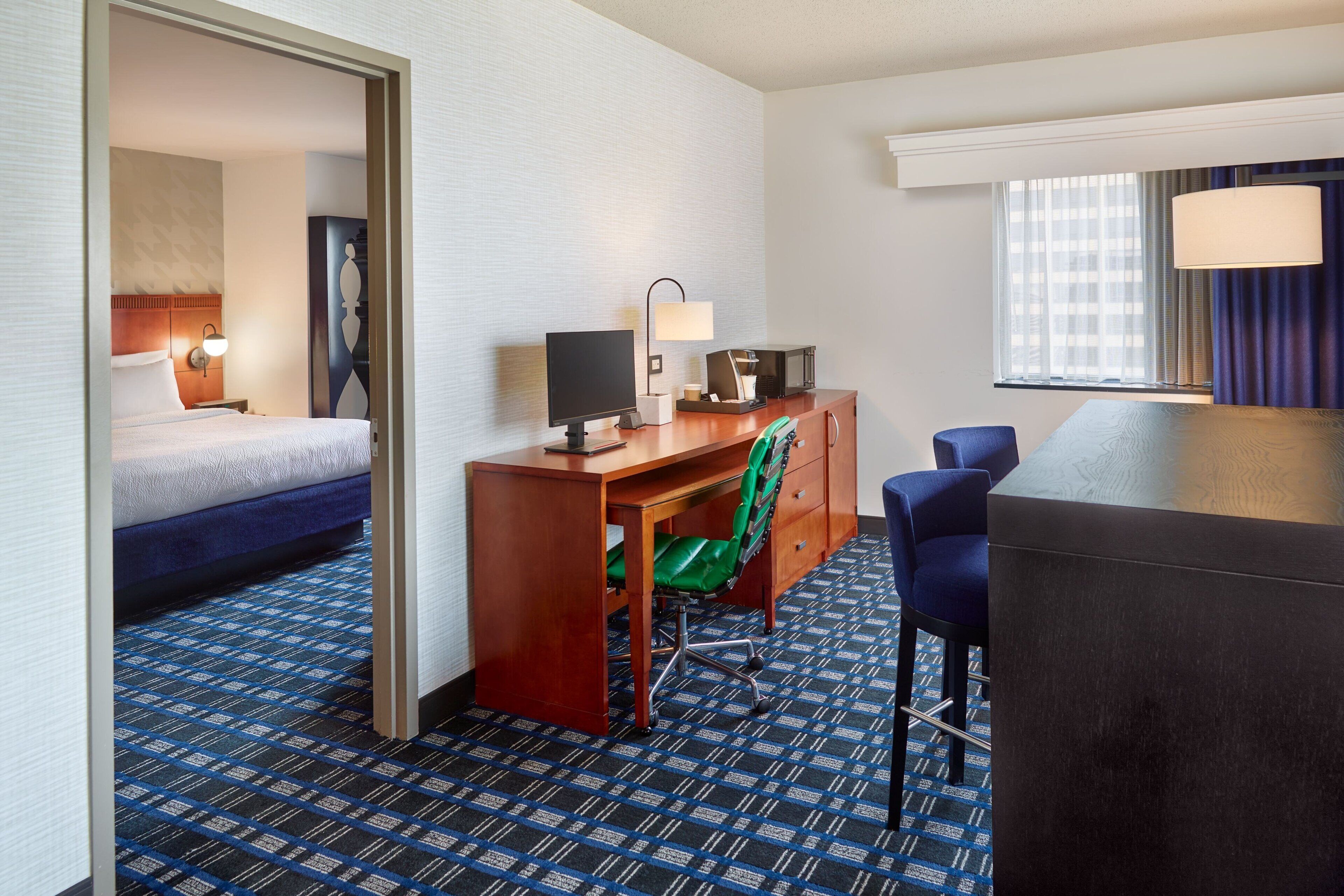 A hotel room with a bed, desk, chair, and a view of the city through the window.