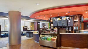 Un vestíbulo moderno de hotel con un mostrador de recepción central, un expositor refrigerado y una zona de estar con mesas y sillas.