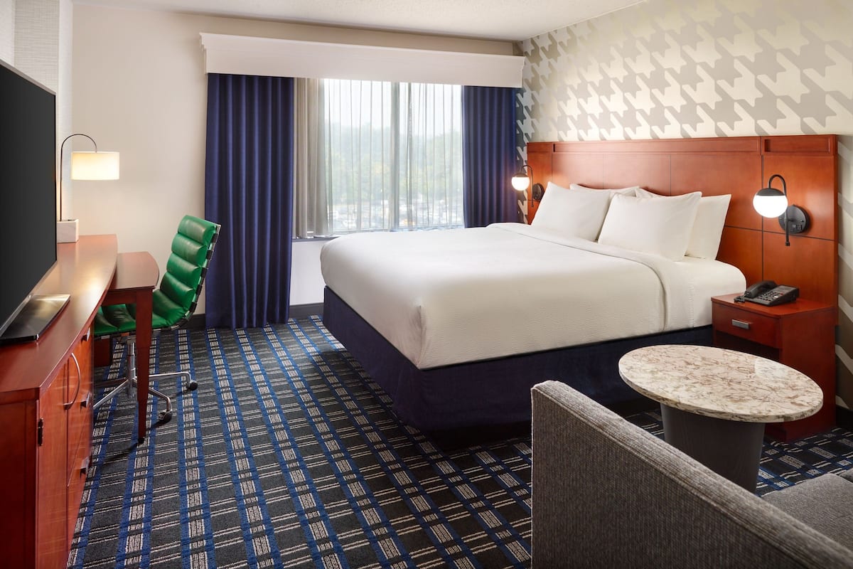 Une chambre d’hôtel avec un grand lit, un bureau avec une chaise, une table ronde et un téléviseur.