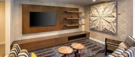 Una sala de estar moderna con un televisor de pantalla plana, estanterías de madera, un tapete estampado y un sofá con cojines a rayas.