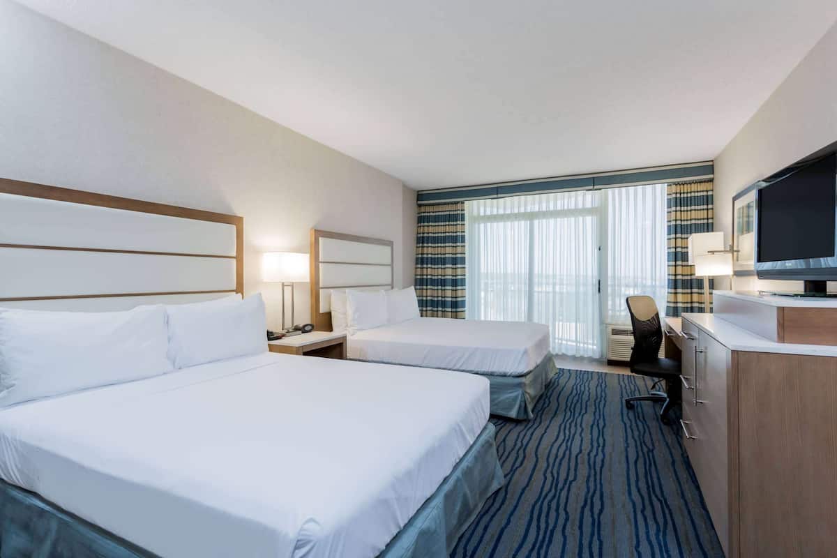 Habitación de hotel con dos camas, un escritorio, televisor y ventana con cortinas.
