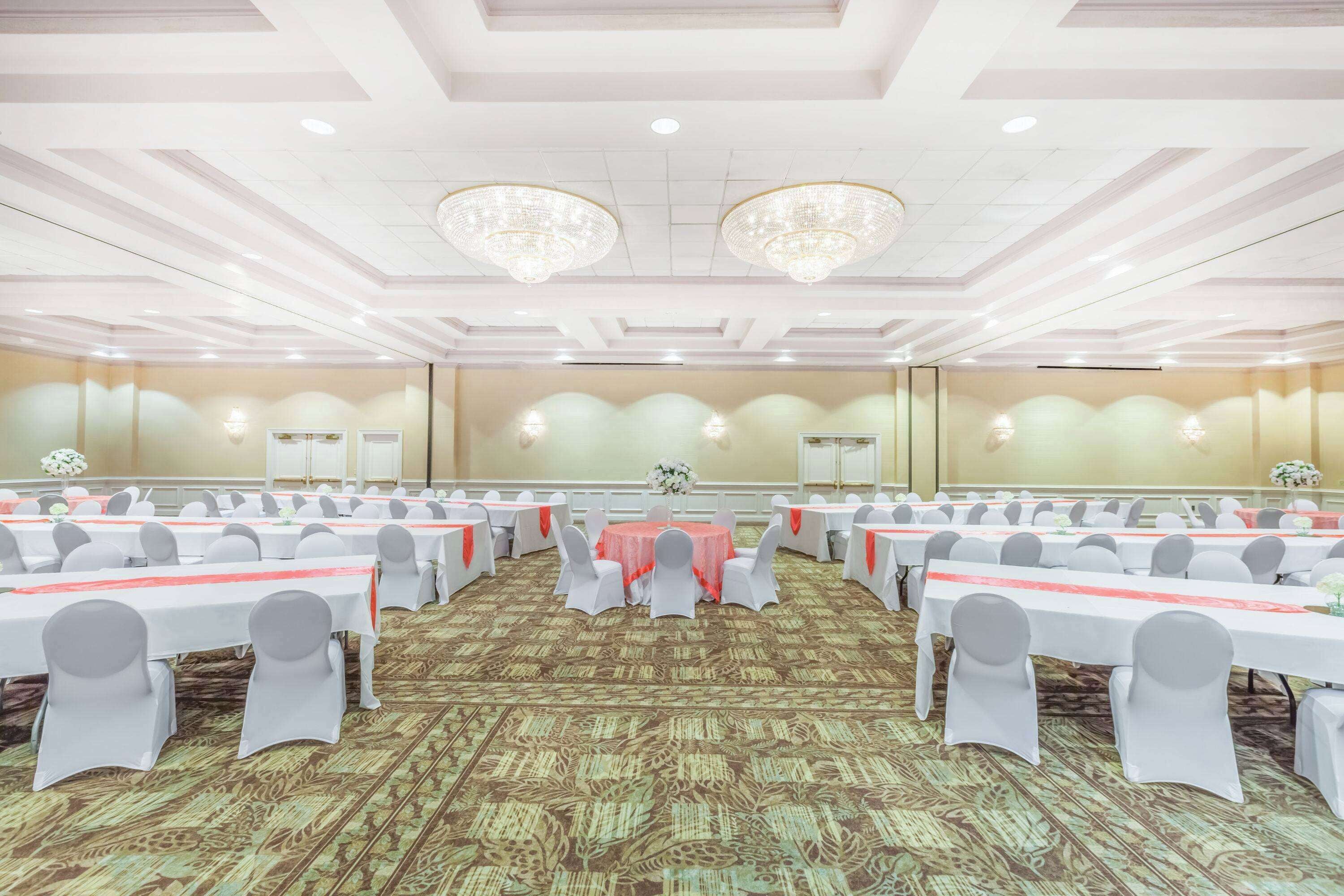 A banquet hall with round tables, white chairs, and a carpeted floor.