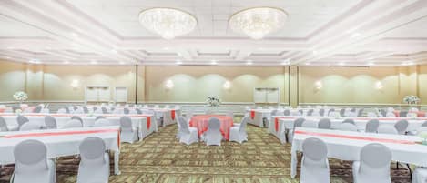 A banquet hall with round tables, white chairs, and a carpeted floor.