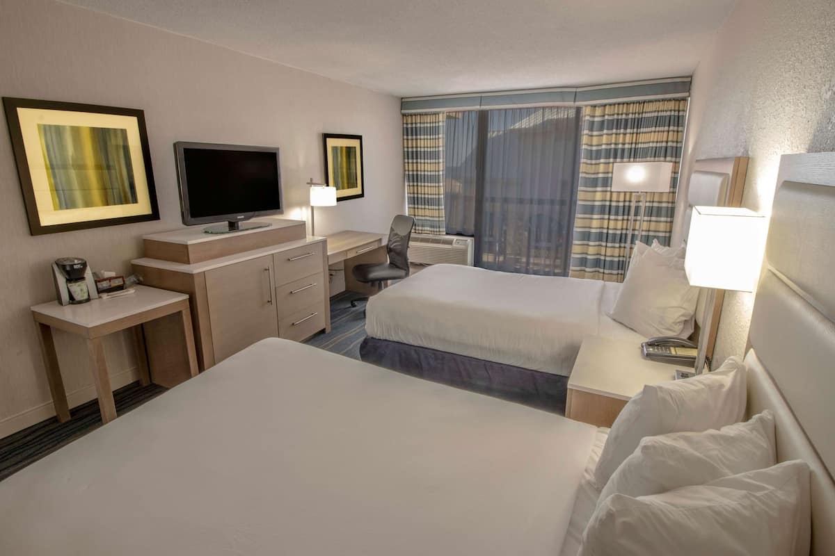 Habitación de hotel con dos camas, un escritorio, un televisor y una ventana con cortinas.