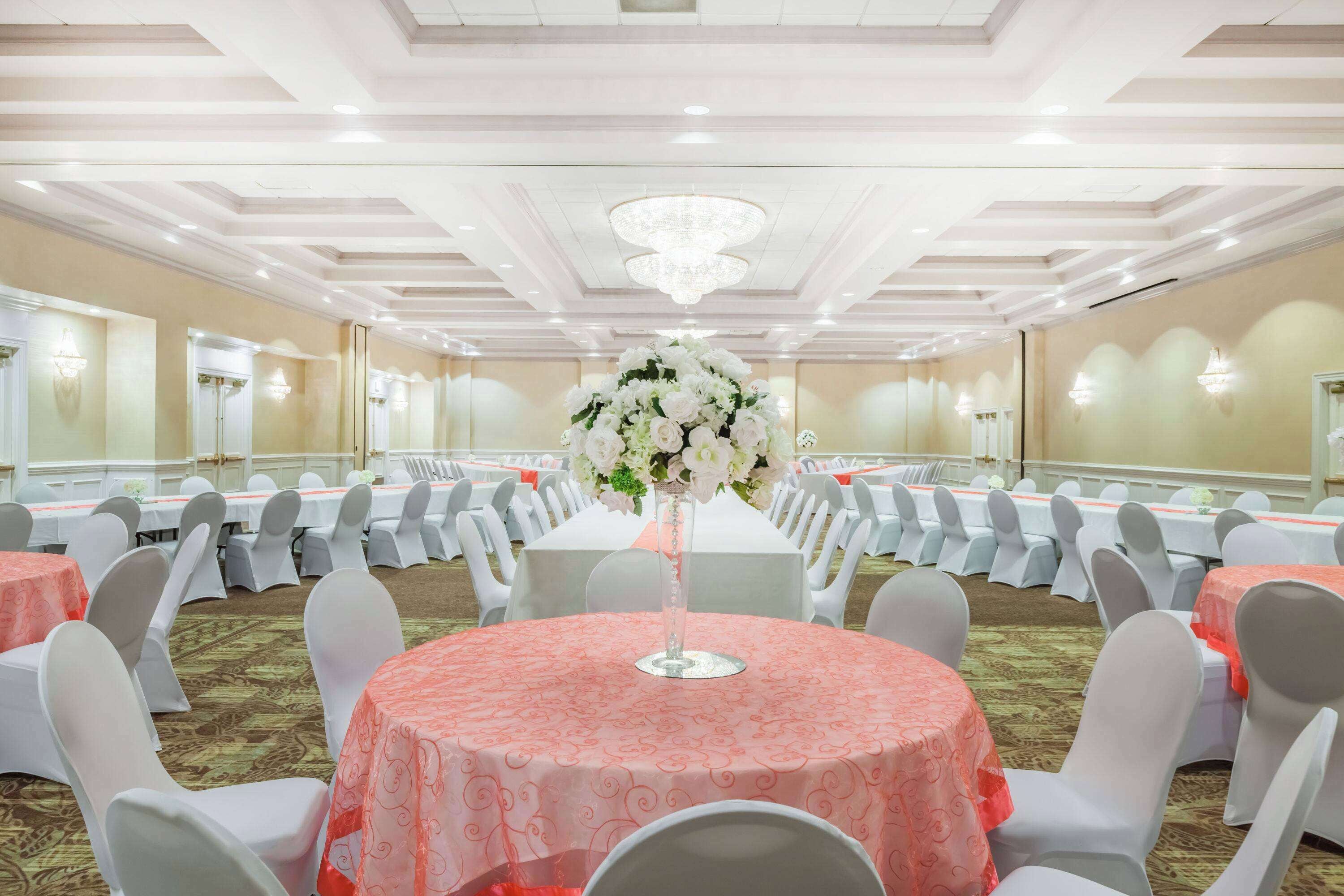 A banquet hall with round tables covered in pink tablecloths, white chairs, and a central floral arrangement.