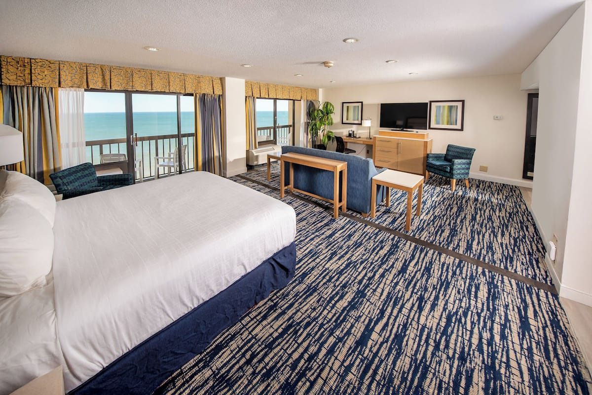 Habitación de hotel con una cama grande, un escritorio, una silla, un televisor y vista al océano.