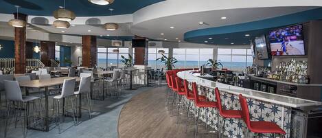 A modern bar area with a curved counter, red bar stools, and a large TV screen.
