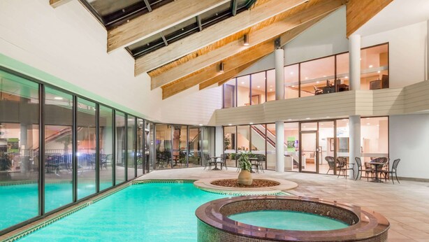 Una piscina interior amb un banyera d'hidromassatge, parets de vidre i un nivell superior amb seients.