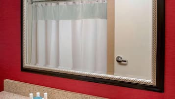 A bathroom with a large mirror, a sink, a towel dispenser, and a shower curtain.