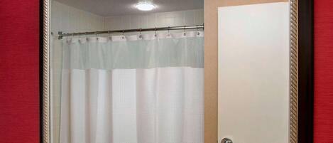 A bathroom with a large mirror, a sink, a towel dispenser, and a shower curtain.