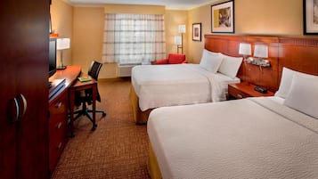 A hotel room with two beds, a desk, a chair, a lamp, and a window with curtains.