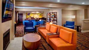 A hotel lobby with a fireplace, a TV, a sofa, a coffee table, and a seating area with chairs and a lamp. - Sonesta Select Boston Danvers (Danvers)