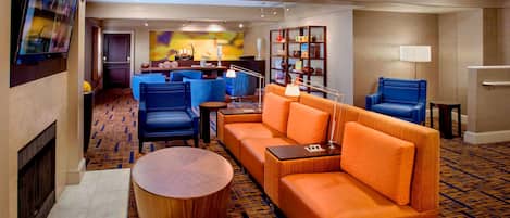 Et hotel lobby med pejs, fjernsyn, sofa, sofabord og en siddeplads med stole og en lampe.