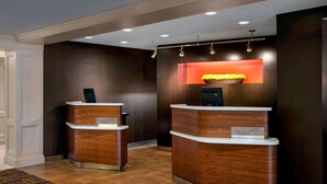 A reception area with two wooden reception desks, a dark wall, and a recessed orange light above the desks. - Sonesta Select Boston Danvers (Danvers)