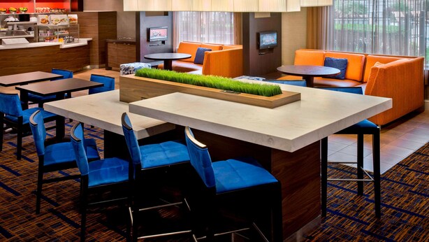 A hotel lobby with a dining area, orange seating, and a TV screen. - Sonesta Select Boston Danvers (Danvers)