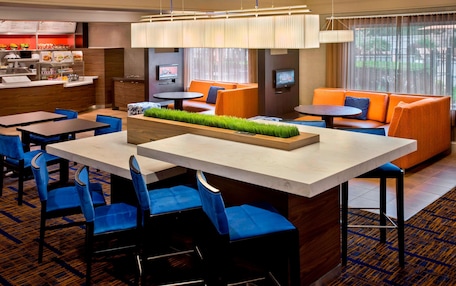 A hotel lobby with a dining area, orange seating, and a TV screen.