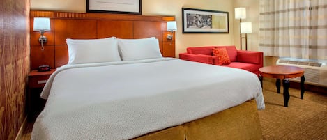 A hotel room with a large bed, a red sofa, a small table, and two wall-mounted lamps.