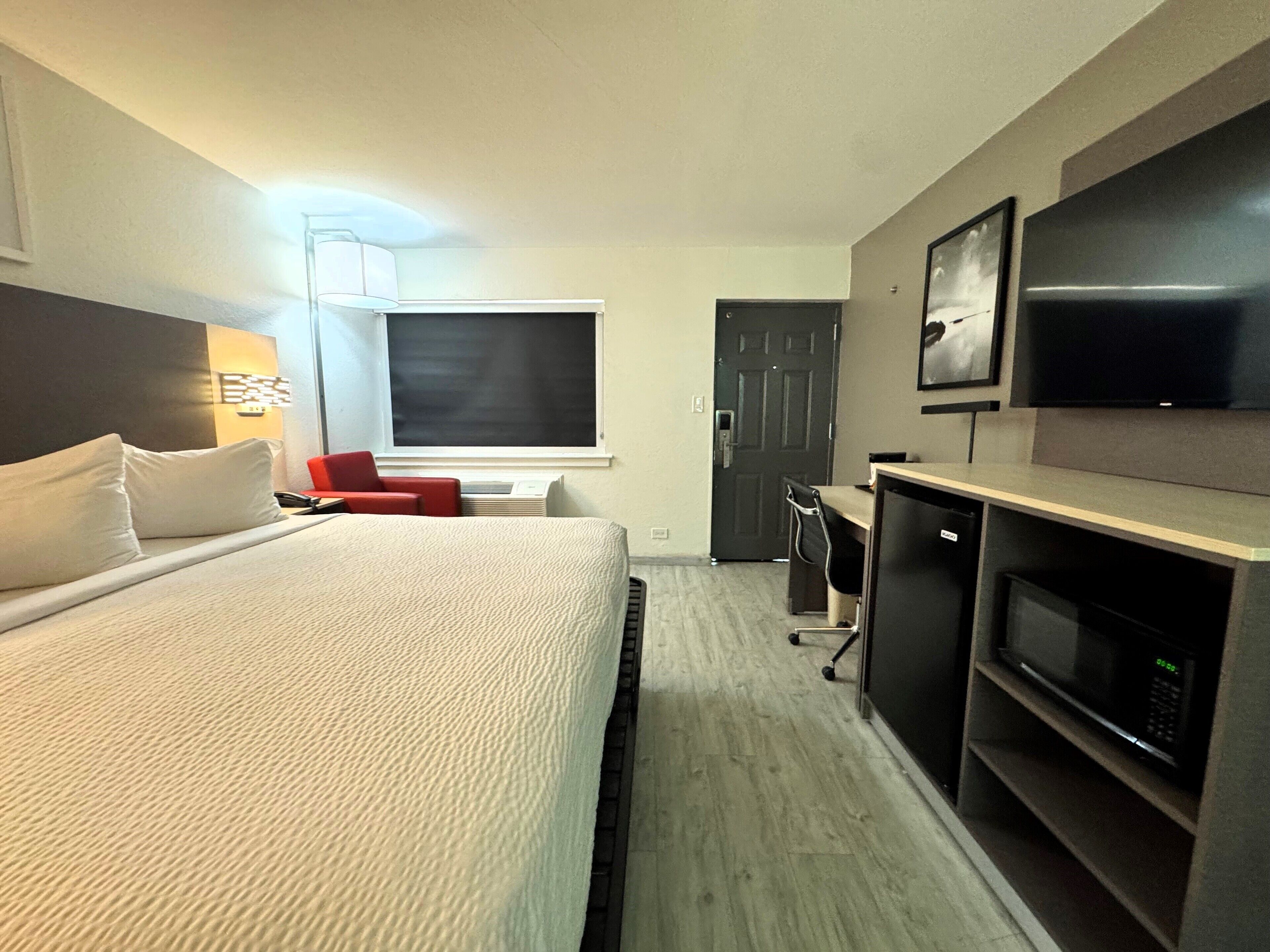 A hotel room with a bed, a desk with a computer, a TV, and a microwave.