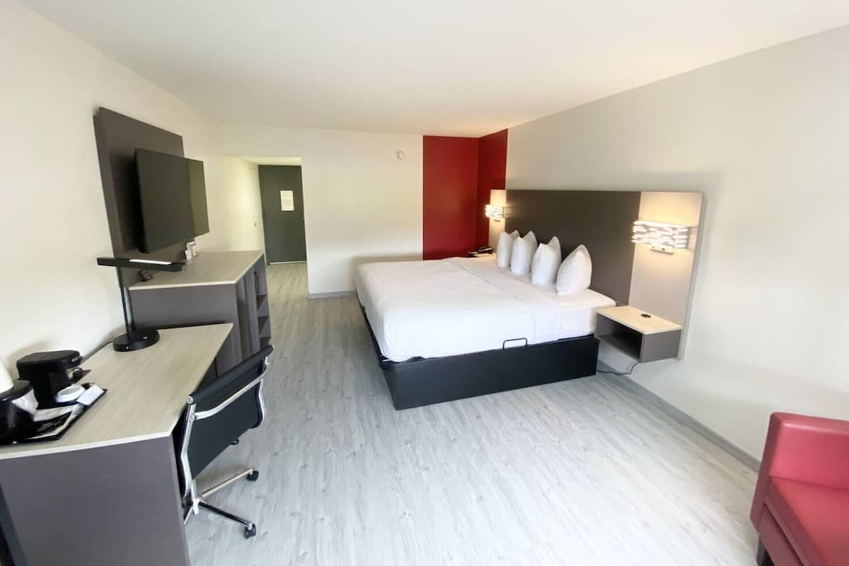 Ett modernt hotellrum med en säng, ett skrivbord med en dator, en tv och en röd accentvägg.
