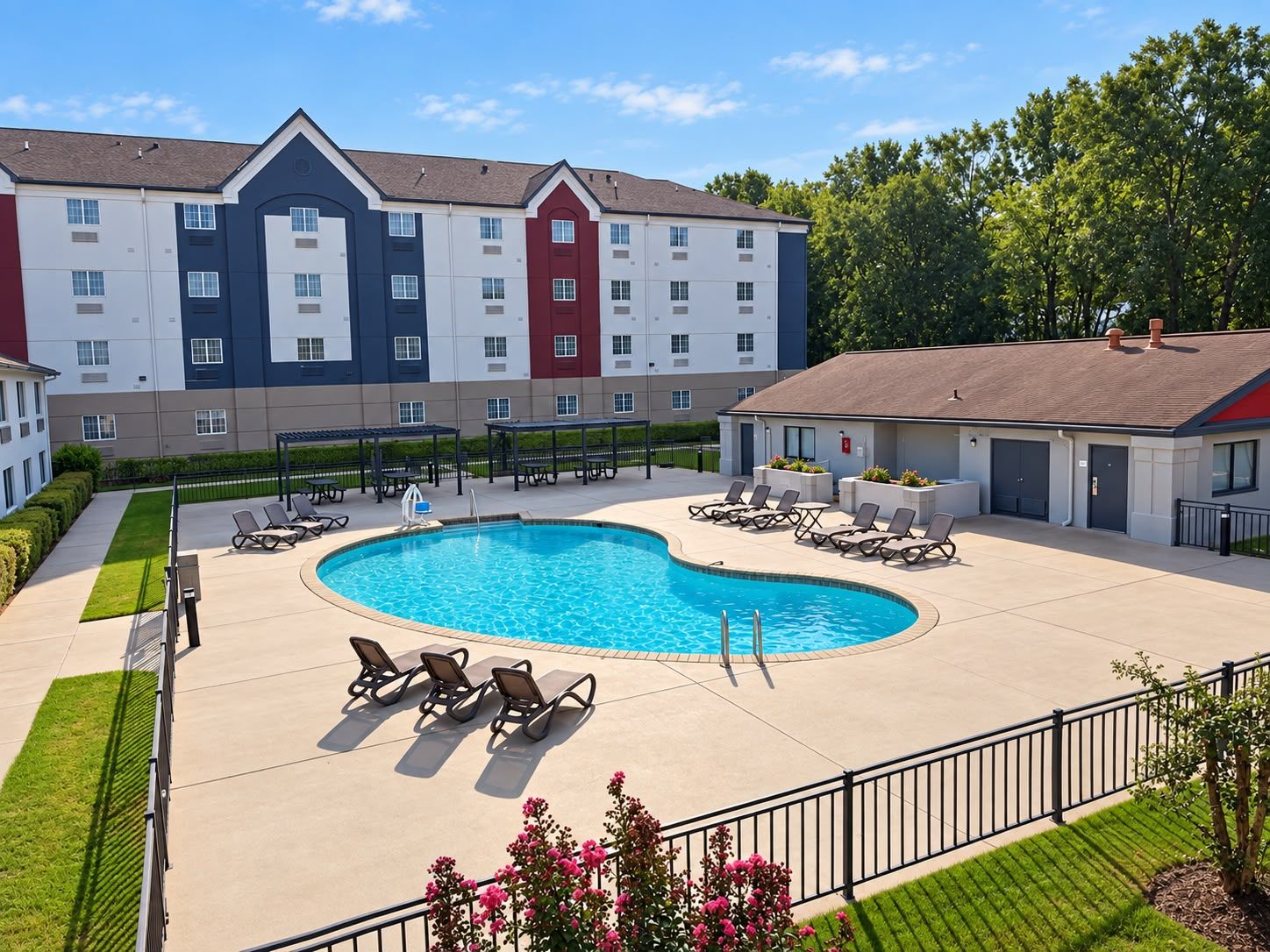 A hotel with a swimming pool, lounge chairs, and a well-maintained lawn.