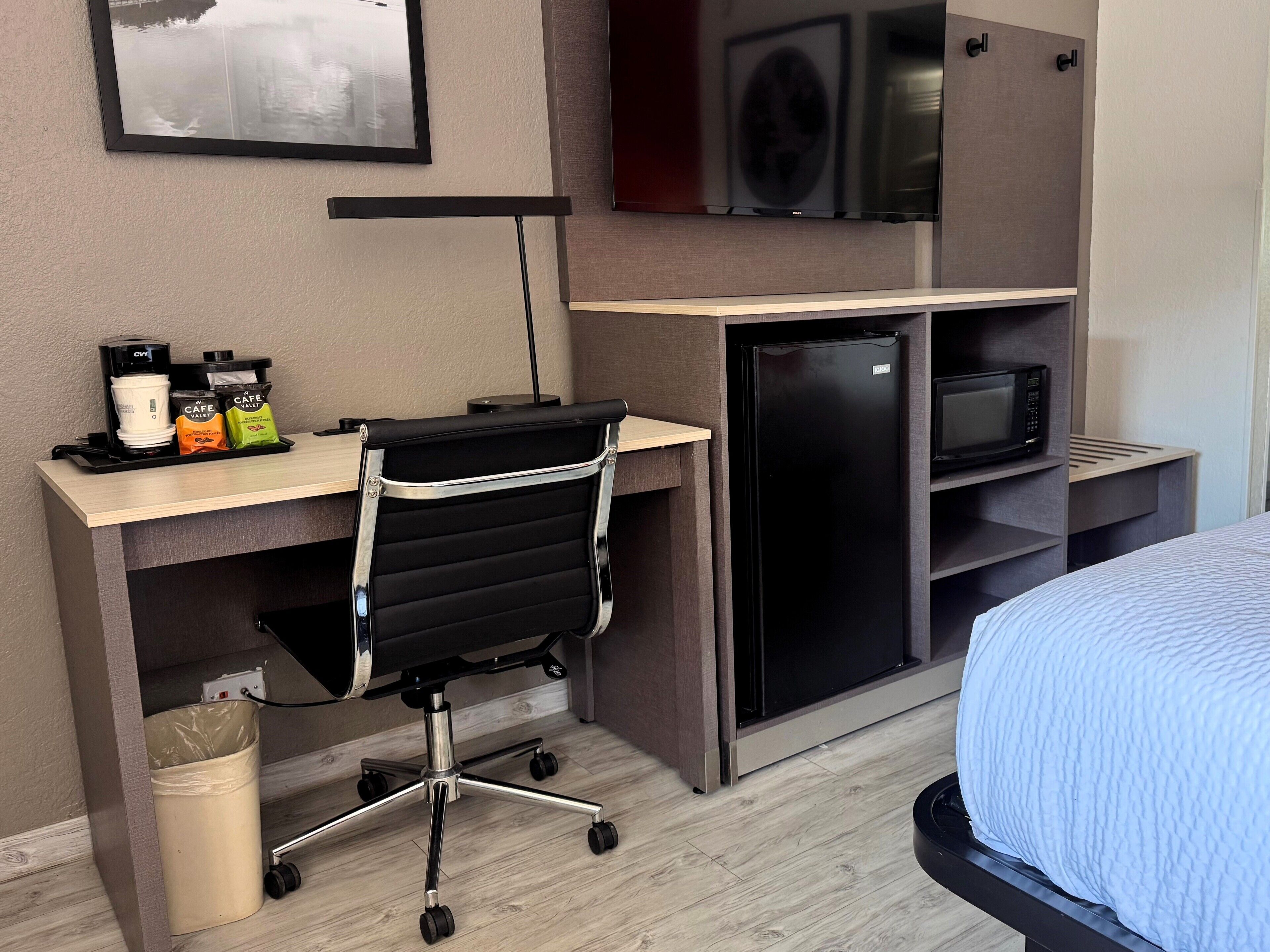 A hotel room with a desk, office chair, microwave, and a bed with a blue quilt.