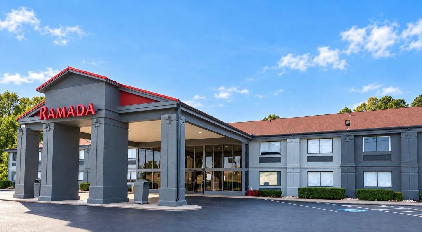 A modern building with a prominent 'RAMADA' sign, large windows, and a covered entrance area.