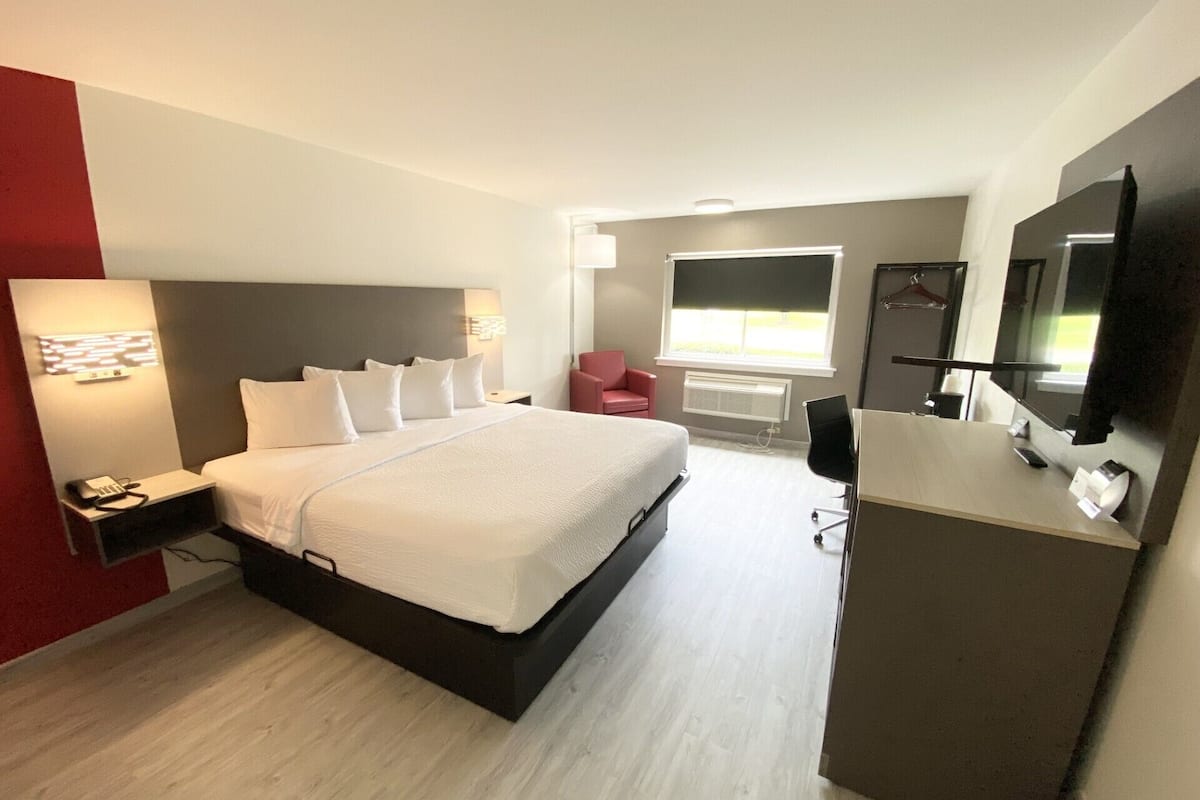 Ett modernt hotellrum med en stor säng, sängbord, ett skrivbord, en stol, en spegel och ett fönster med utsikt.