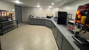 A kitchen area with a counter, microwave, and a refrigerator. There are various food items and condiments on the counter.