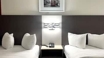 A hotel room with two beds, a bedside table with a phone, a wall-mounted light, and a framed picture above the bed.