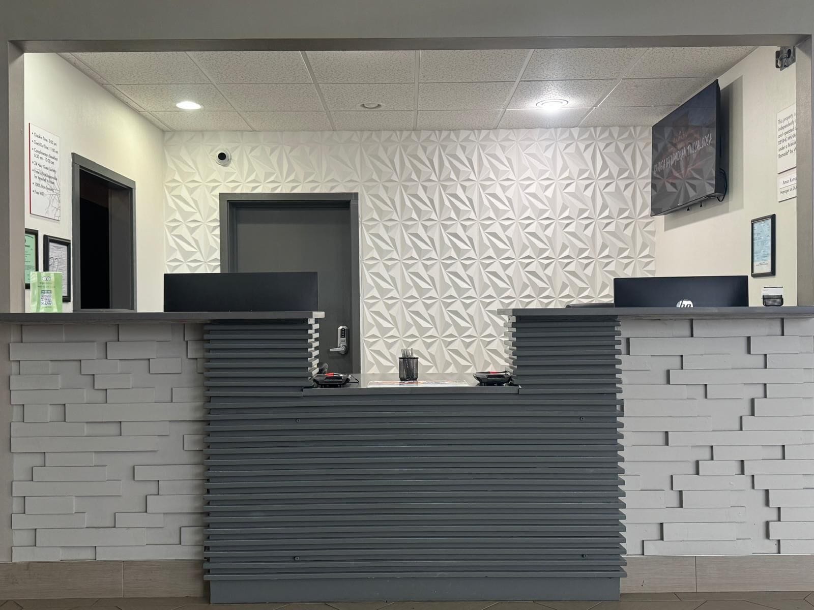 Ein Empfangsschalter mit modernem Design, inklusive einer Wand mit geometrischem Muster und einem Flachbildfernseher.