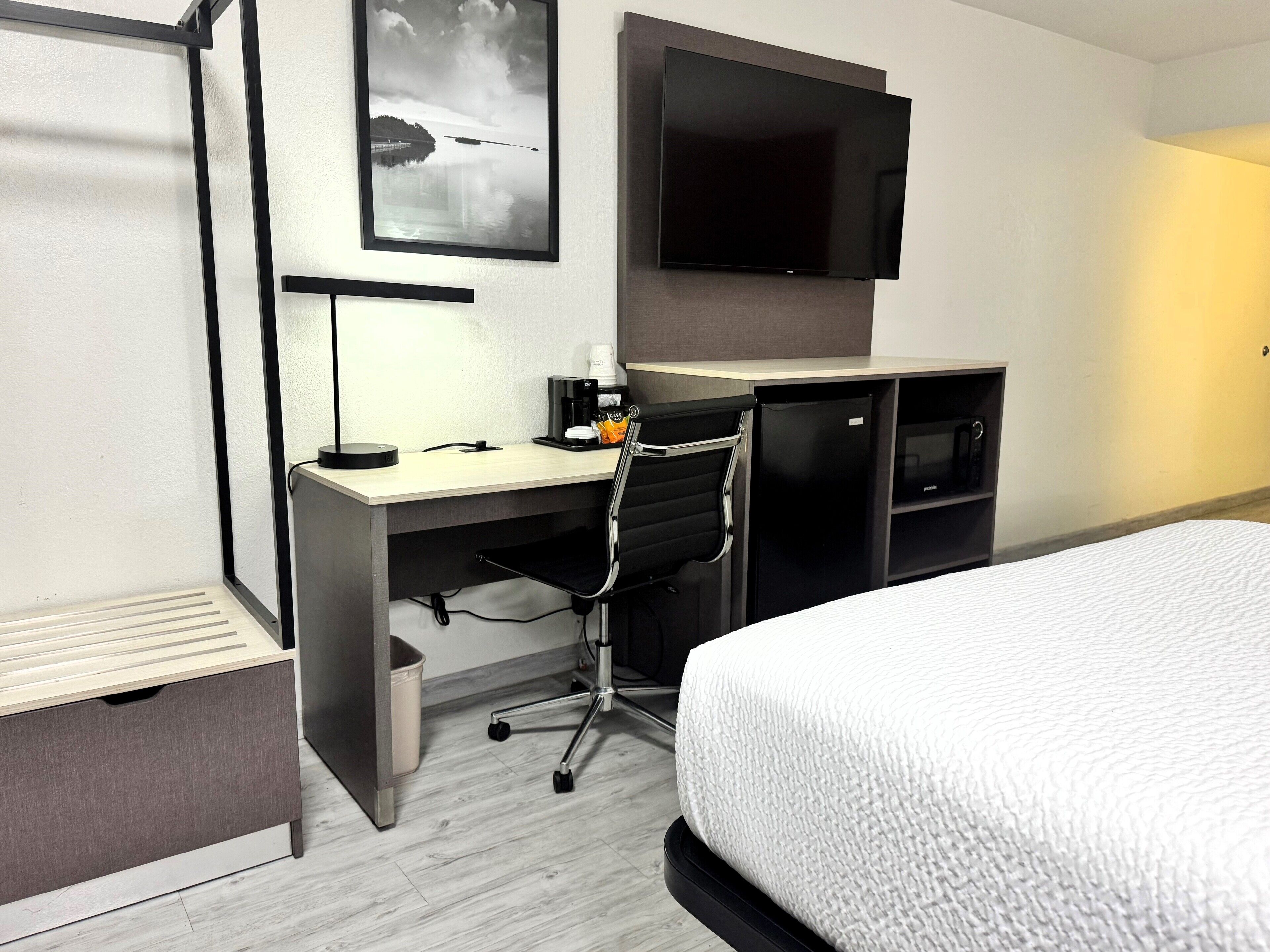 A hotel room with a bed, a desk with a chair, a television, and a coffee maker.