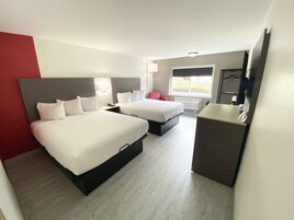 Quarto de hotel com duas camas, uma escrivaninha, uma cadeira, uma televisão e uma janela.