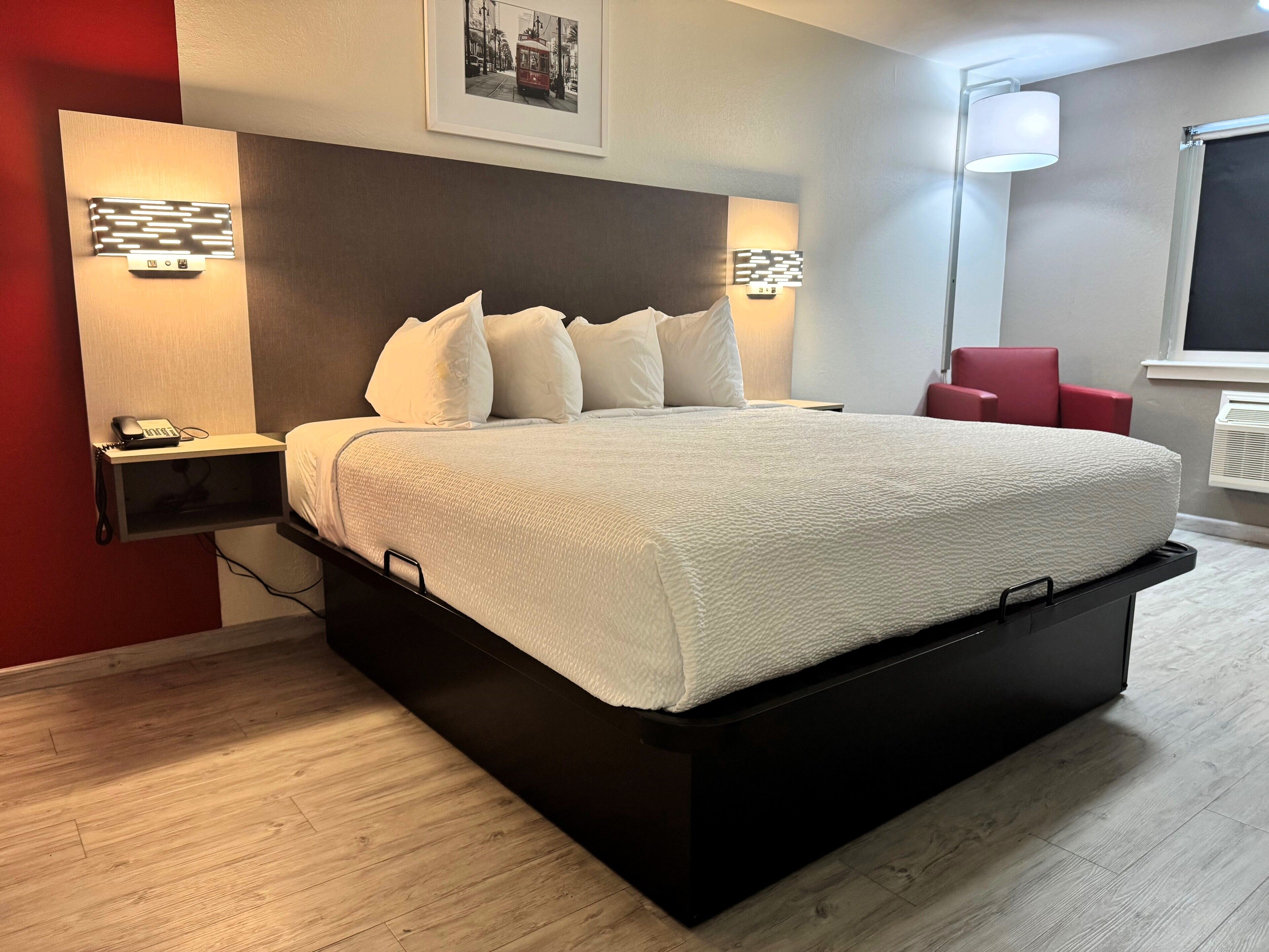 Een moderne hotelkamer met een groot bed, bedlampen, een rode stoel en een ingelijst schilderij aan de muur.