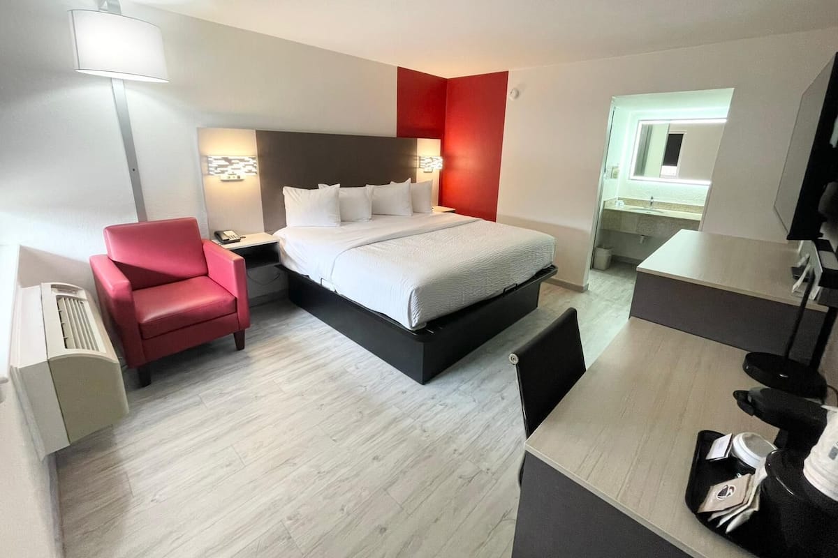 Ett modernt hotellrum med en säng, ett skrivbord, en stol och ett badrum som syns genom en öppen dörr.