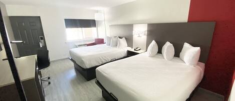 Quarto de hotel com duas camas, uma escrivaninha, uma cadeira e uma janela.