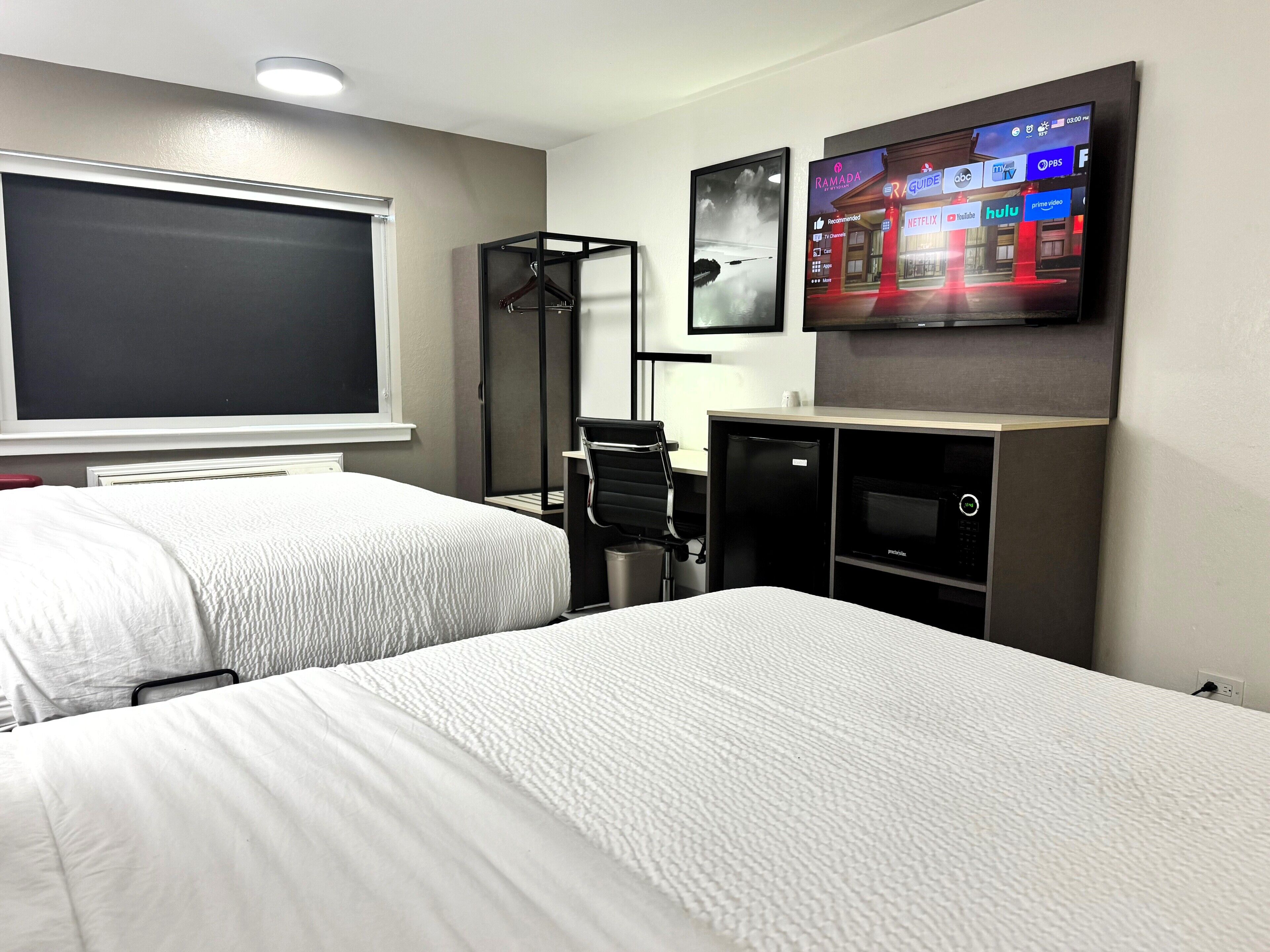 Habitación de hotel con dos camas, un televisor montado en la pared y un escritorio con una silla.