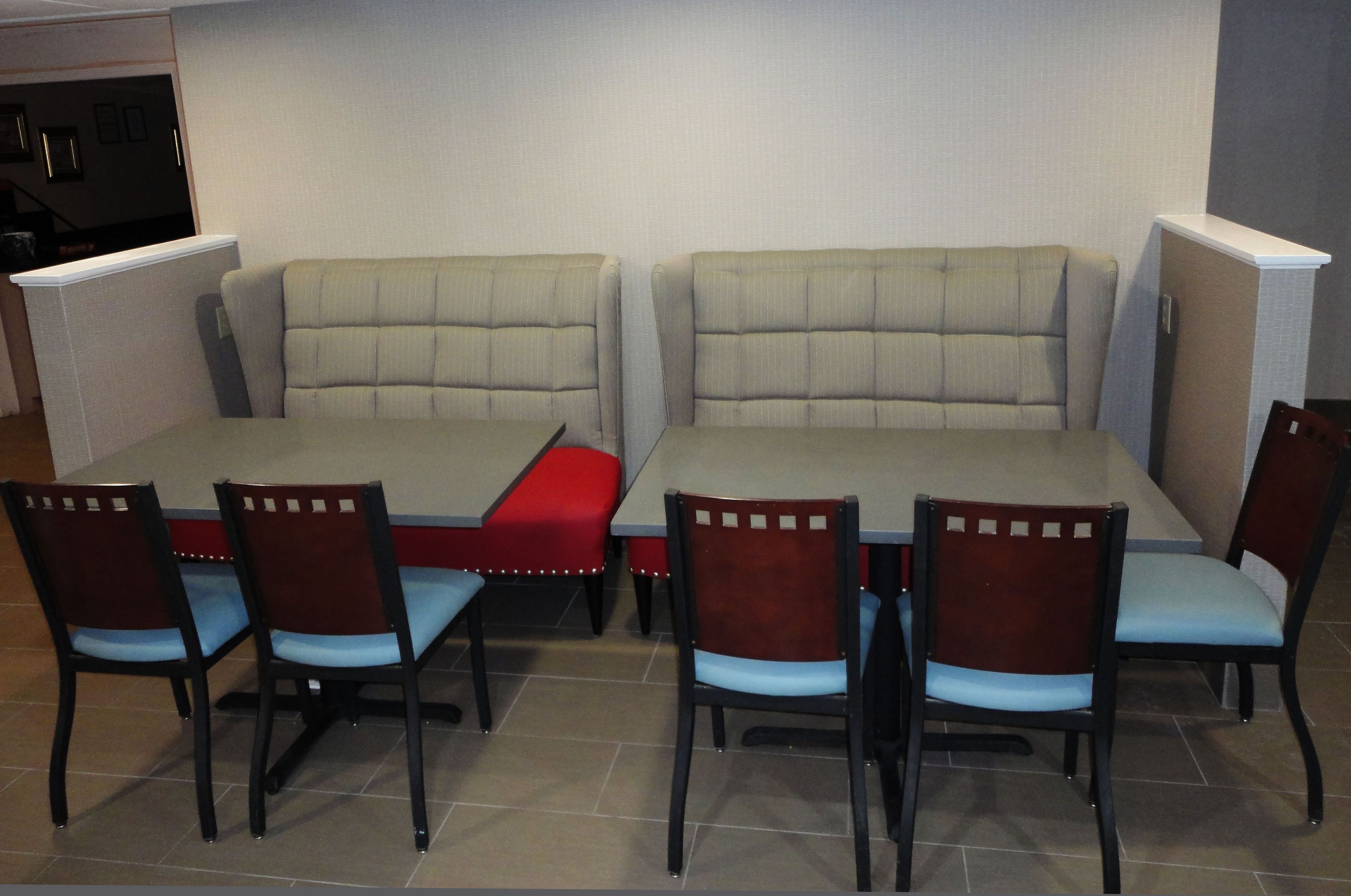 Un comedor con una mesa tipo cabina y sillas, un banco rojo, y una pared con un interruptor de luz.
