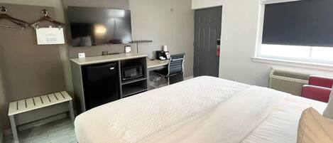 Habitación de hotel con cama, televisión, escritorio con computadora, microondas y refrigerador pequeño.