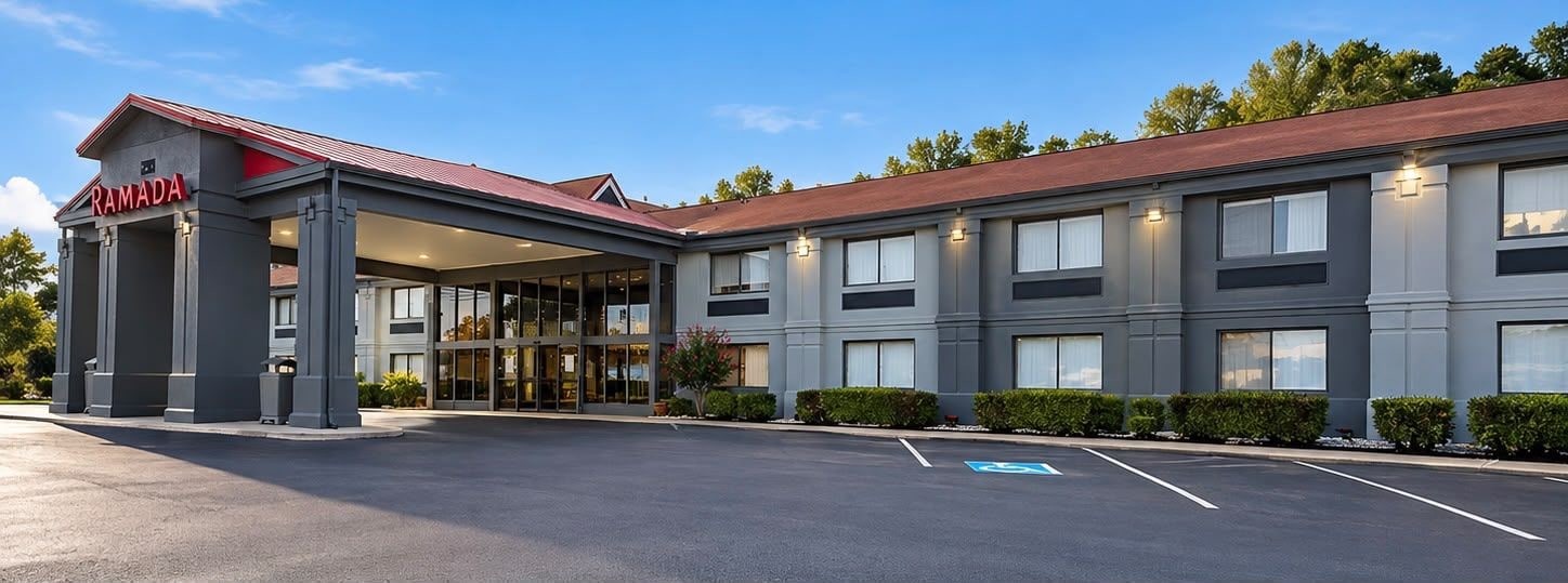 A modern hotel with a covered entrance, a parking lot, and a sign reading 'RAMADA'.