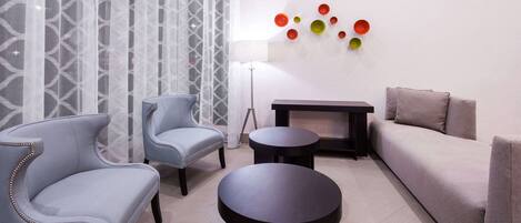 Un salon moderne avec deux fauteuils gris, un canapé gris, deux tables d’appoint noires et un lampadaire.