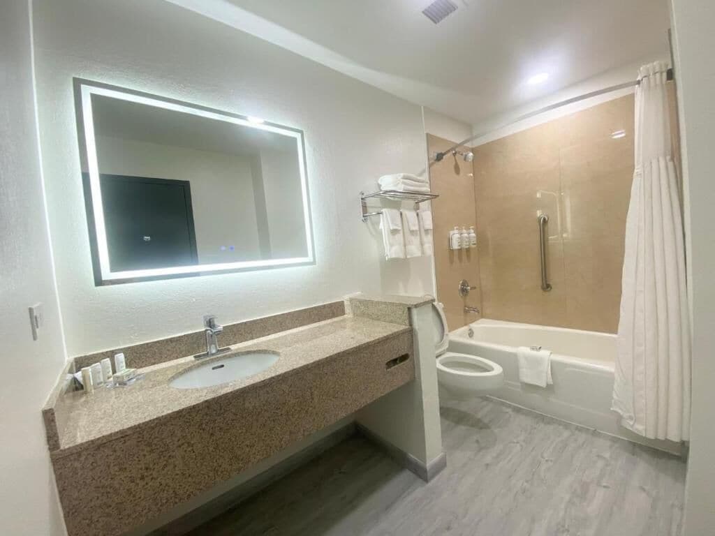 Een moderne badkamer met een grote spiegel, twee wastafels, een douche en een bad.