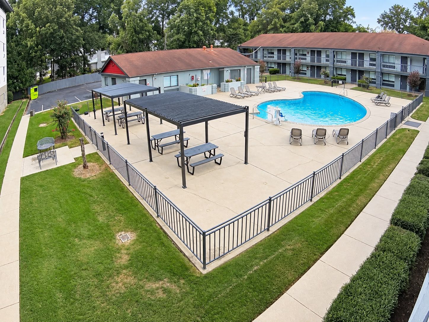A pool area with a covered seating area, lounge chairs, and a building in the background.