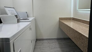 A laundry area with a washing machine, dryer, and a countertop with a sink. - Ramada by Wyndham Tuscaloosa (Tuscaloosa)