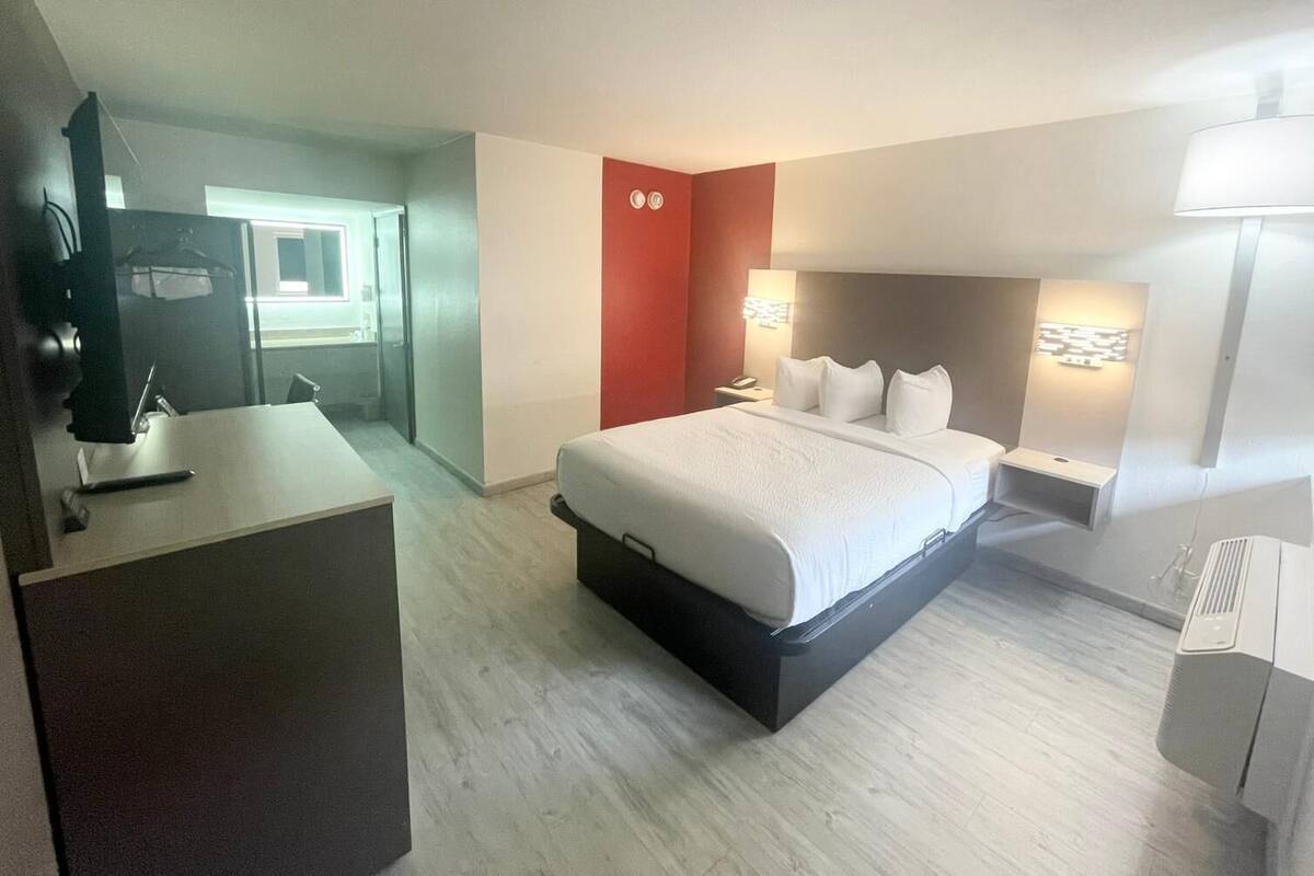Ett hotellrum med en säng, ett nattduksbord, en lampa och ett skrivbord med en stol.