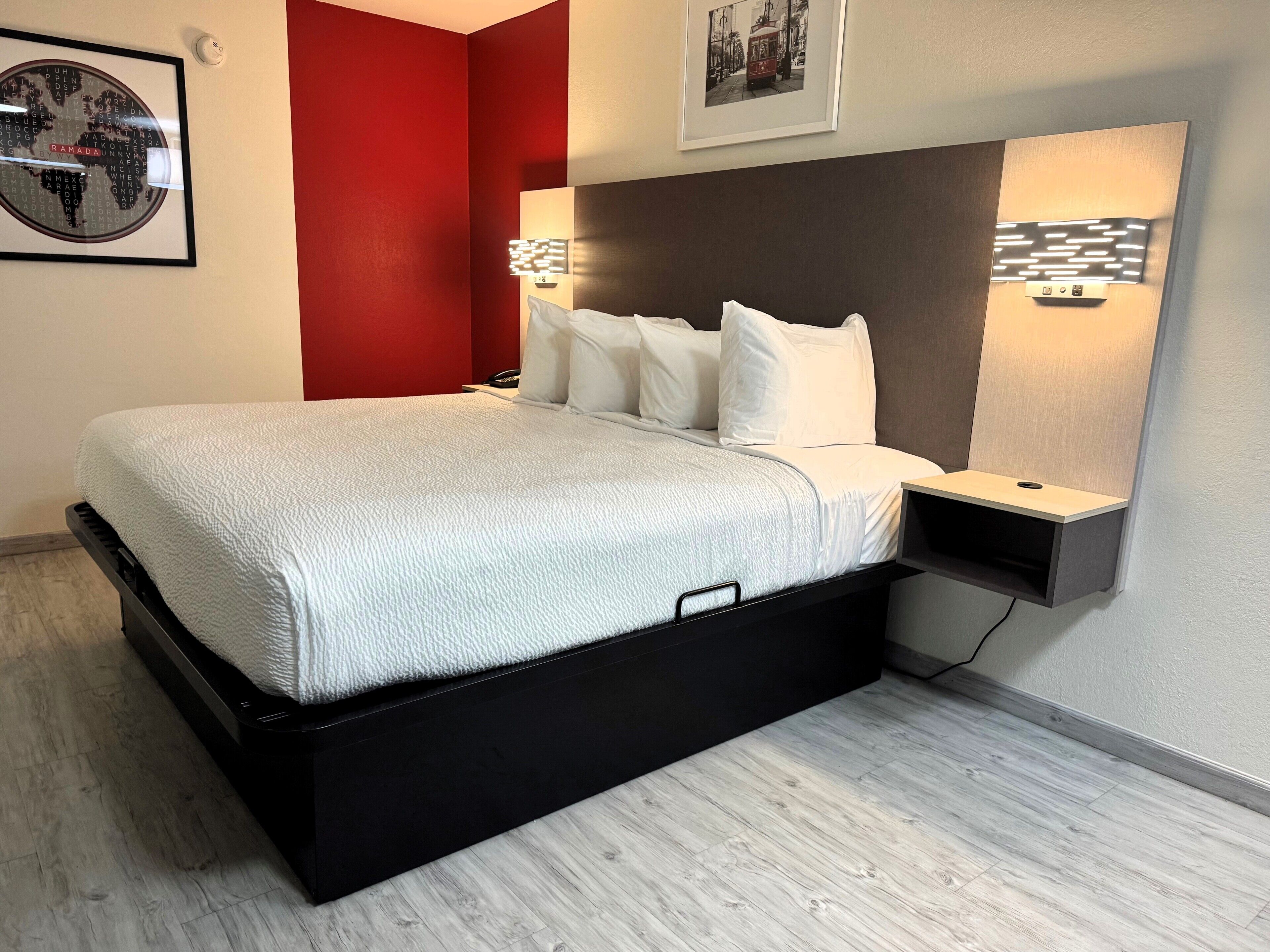 Camera d'albergo moderna con un letto, un comodino, una lampada a parete e un quadro con un tram.